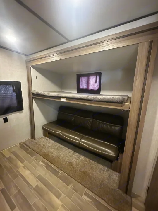 RV rental interior featuring bunk beds: an upper bed with a grey mattress and a lower brown sofa, on wood-look flooring.. Crossroads RV Zinger 2020