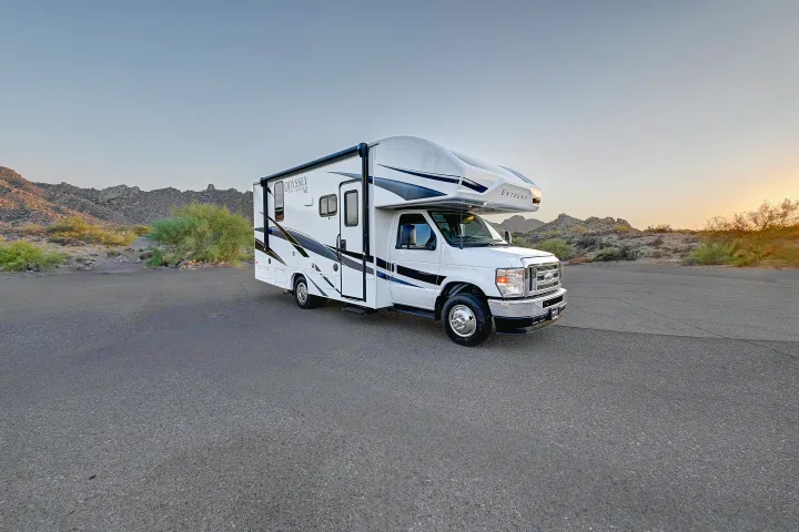 White Entegra Odyssey RV rental parked on asphalt, set against a desert landscape with mountains at sunset.. Entegra Coach Odyssey SE 2024