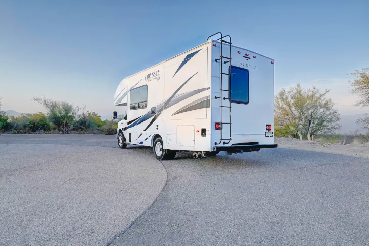White Odyssey Entegra Class C RV, perfect for your next rv rental road trip, parked on asphalt surrounded by desert landscape.. Entegra Coach Odyssey SE 2024