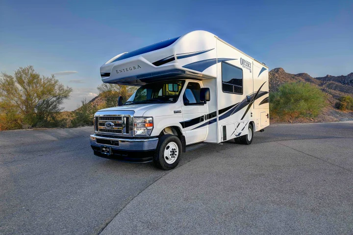 White Entegra Odyssey Class C RV rental on a desert road, mountains & blue sky backdrop. Perfect for trips!. Entegra Coach Odyssey SE 2024
