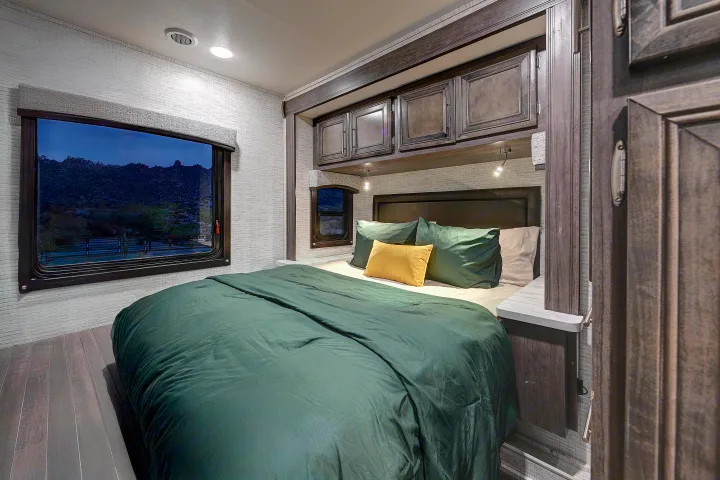 RV rental bedroom with dark green bed, overhead cabinets, and large window with night view. Ideal for your next trip.. Entegra Coach Odyssey SE 2024