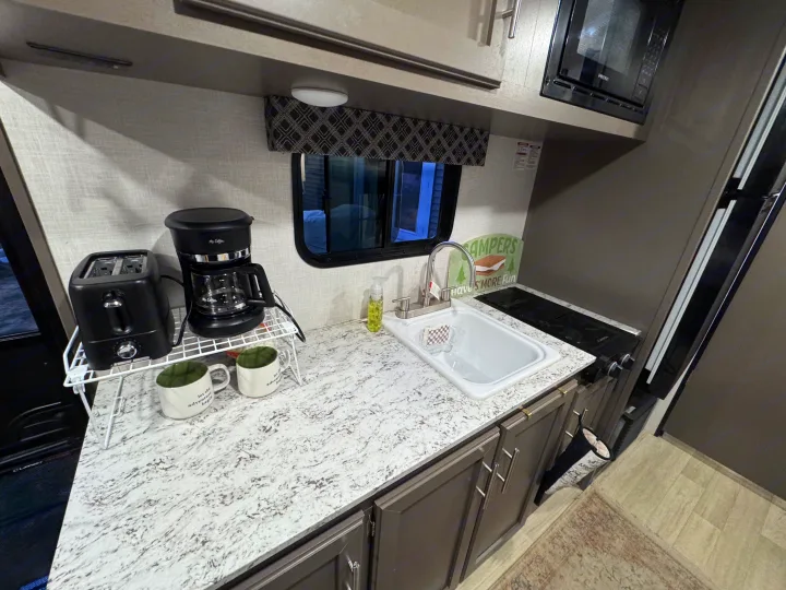 Modern RV rental kitchen with coffee maker, toaster, sink, stove, and microwave. Perfect for camping adventures.. KZ Sportsman 2024