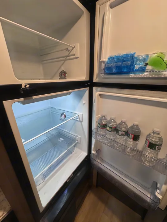 Open RV rental refrigerator showcasing spacious interior with freezer, ice packs, and bottled water on door shelves.. KZ Sportsman 2024