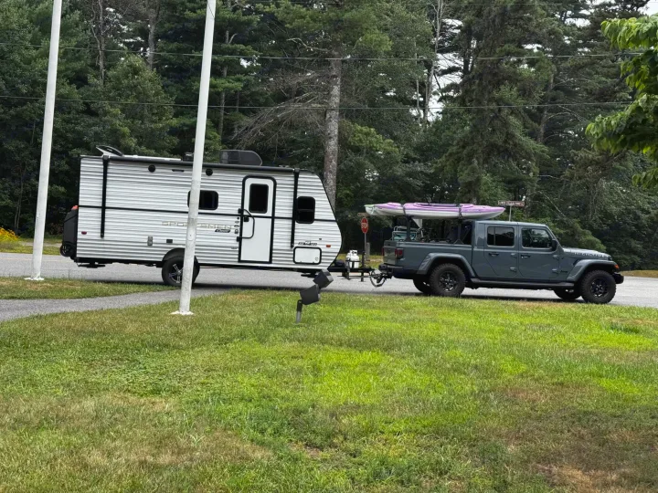Explore with this RV rental setup: a gray Jeep Gladiator towing a white travel trailer & kayaks for your next adventure.. KZ Sportsman 2024