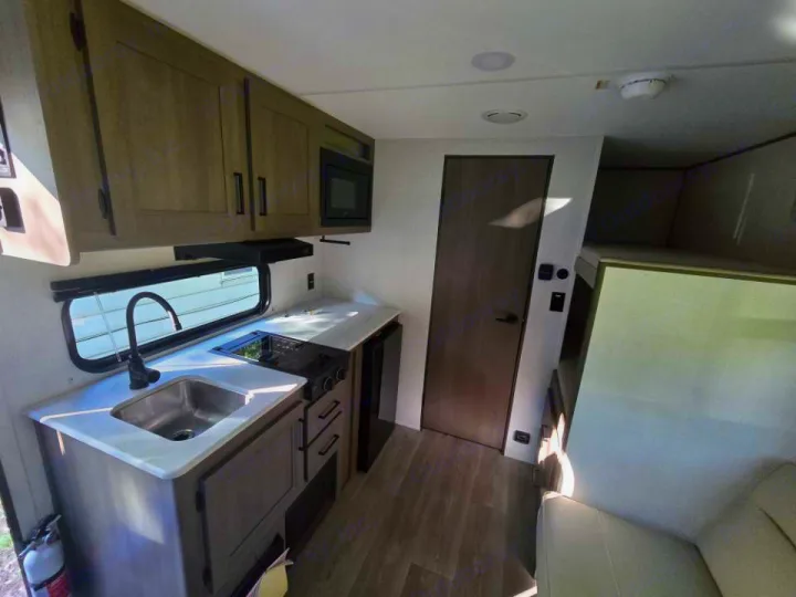 Inside this RV rental: a compact, modern kitchen with sink, stove, and microwave, plus cozy living/sleeping areas.. Grand Design 151BH 2025