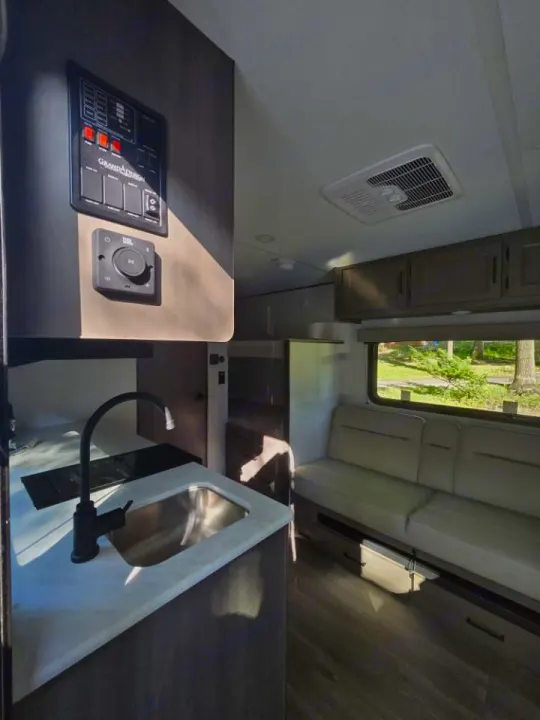 Modern RV rental interior showing a clean kitchen with sink, cozy sofa seating, and a control panel. Perfect for your next trip!. Grand Design 151BH 2025