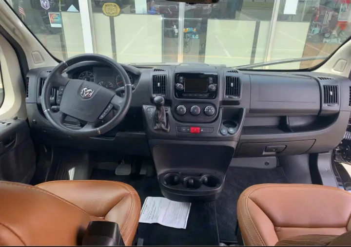 This RV rental's cockpit shows the black steering wheel with a Ram logo, dashboard controls, and tan leather front seats.. Dodge Sprinter 2500 170ext 2021
