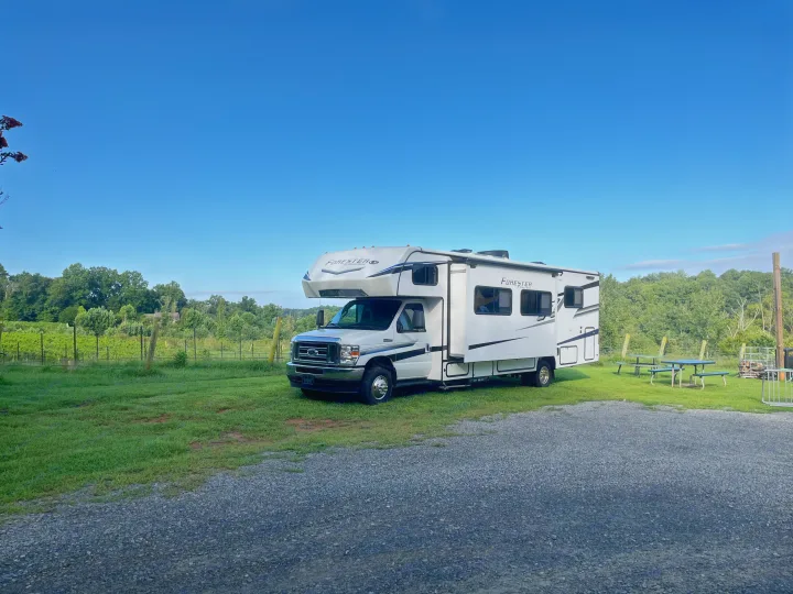 White Forester RV rental parked in a vineyard campsite with picnic tables under a clear blue sky.. Forest River Forester 2024