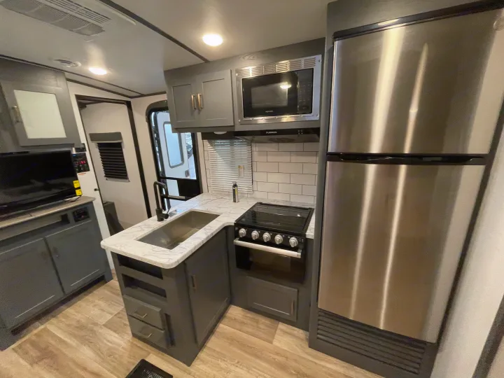 Well-equipped RV rental kitchen with stainless steel fridge, stove, microwave, and sink, alongside modern grey cabinets.. Keystone RV Bullet Ultra Lite 2022