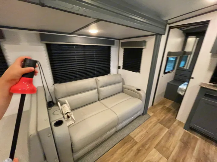 RV rental interior: Gray reclining sofa with cup holders, black window blinds, and wood-look flooring in a modern setup.. Keystone RV Bullet Ultra Lite 2022