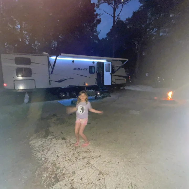 A joyful girl dances by an illuminated RV rental and a warm campfire at a night campsite. Ideal for family fun!. Keystone RV Bullet Ultra Lite 2022