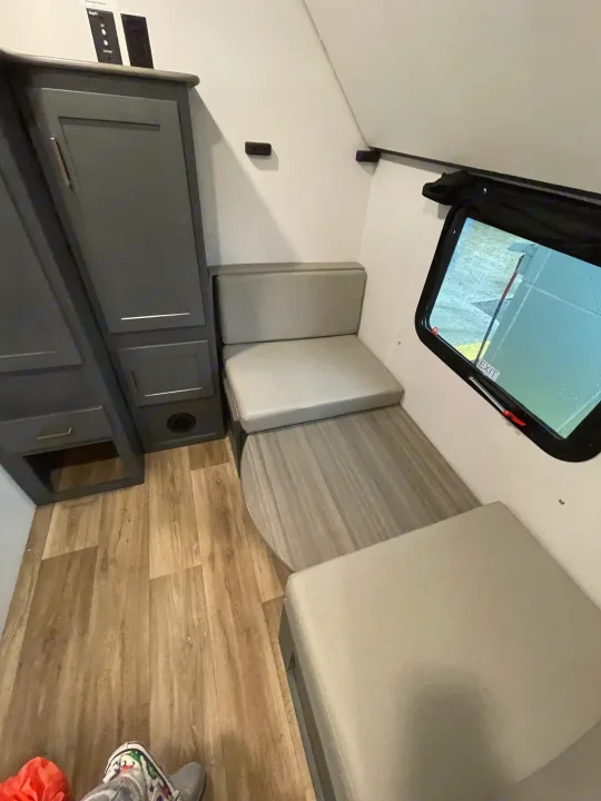 Cozy RV rental dinette featuring grey cushions, wood-look table, cabinet storage, and a safety exit window.. Keystone RV Bullet Ultra Lite 2022