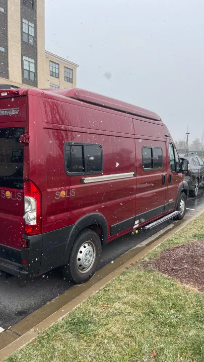 Red Winnebago Solis van RV rental parked on an overcast, snowy day with a modern building in the background.. Winnebago Solis 2023