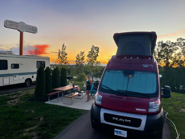 Sunset at Kings Island Camp Cedar: an RV rental van and motorhome parked, with people at a picnic table.. Winnebago Solis 2023