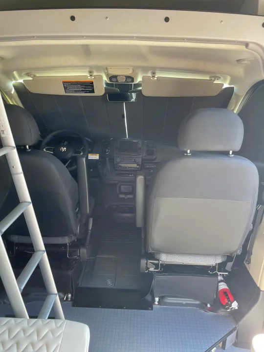 Front cabin of an RV rental van, featuring seats, dashboard, sunshade, and a visible fire extinguisher.. Winnebago Solis 2023