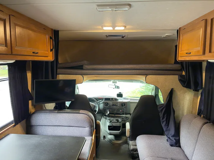 An rv rental interior looking forward: dinette, TV, cockpit, and an overhead bunk with cabinets visible.. Other Other 2017