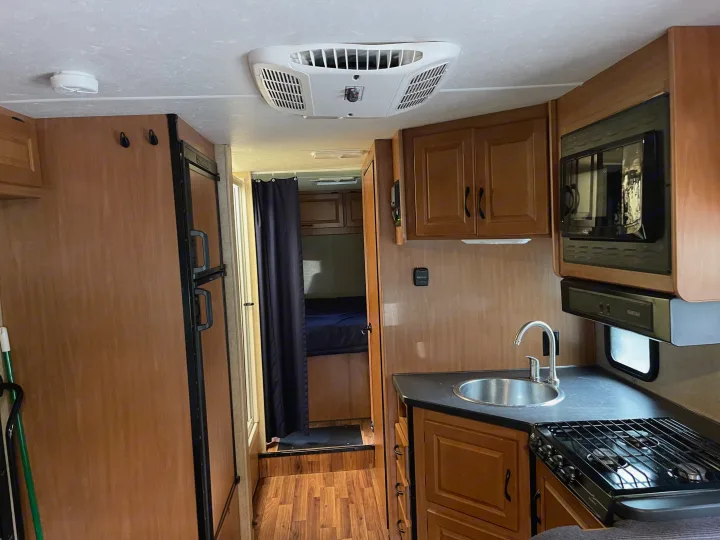 An RV rental interior with a well-equipped kitchen (sink, stove, microwave), refrigerator, and a private bedroom separated by a curtain.. Other Other 2017