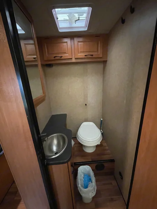 Compact RV rental bathroom features a toilet, sink, mirror, overhead cabinets, and roof vent, optimizing space for travel.. Other Other 2017