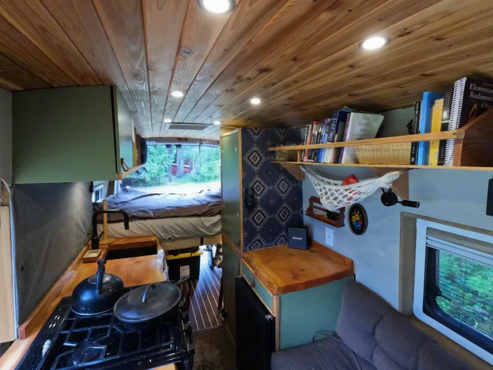 This cozy custom rv rental interior features a wooden ceiling, built-in kitchen, bed, and living area, ideal for travel.. Ford Transit 2017