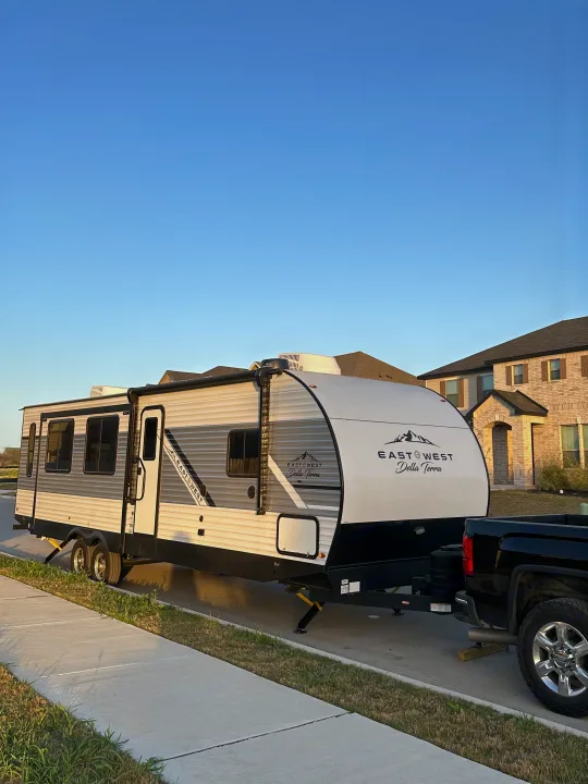 An East to West Della Terra RV rental, hitched to a truck, parked on a suburban street. Ready for adventure!. East to West Della Terra 2024