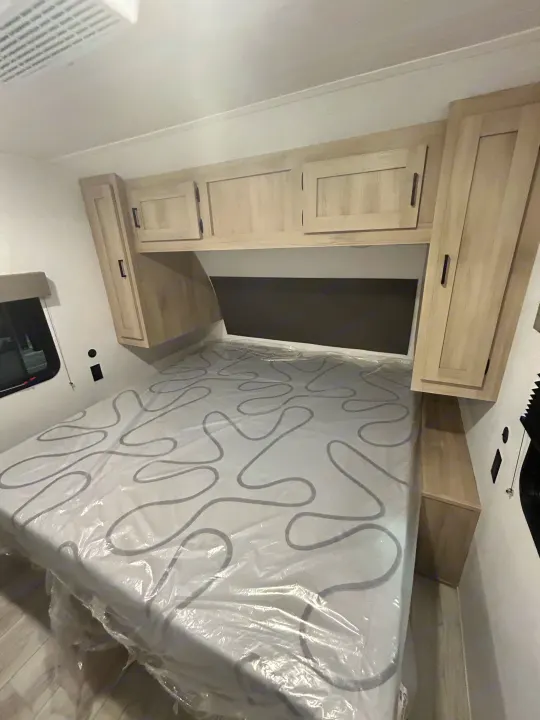 Interior of an RV rental bedroom: new mattress, overhead cabinets, and a window for comfortable stays.. East to West Della Terra 2024