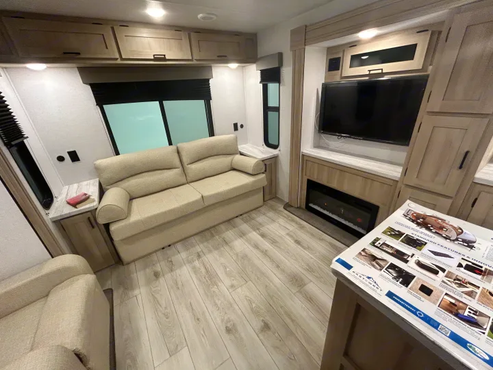 Bright RV living space featuring a sofa, TV, electric fireplace, and storage cabinets. Perfect for your next rv rental adventure.. East to West Della Terra 2024