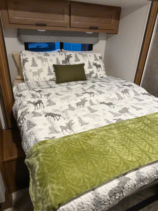Relax in this RV rental's cozy bedroom featuring a moose-themed quilt, green throw, and wood-grain cabinets.. Forester LE 2022