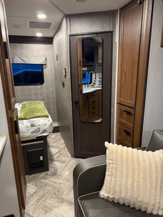 Inside a modern RV rental: a comfy bed, wood-look flooring, and a mirrored door reflecting the functional kitchen space.. Forester LE 2022