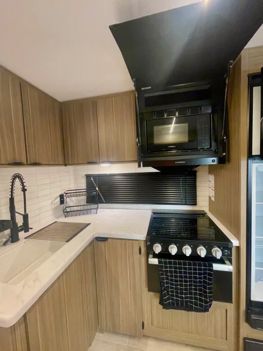 RV rental kitchen: light wood cabinets, white sink, black microwave & stove, and white tile backsplash.. Forest River Salem 29BDB 2025