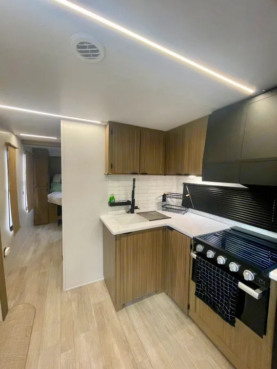 Modern RV rental's kitchen and living space, featuring a stove, sink, wood cabinets, and bright ceiling lights.. Forest River Salem 29BDB 2025