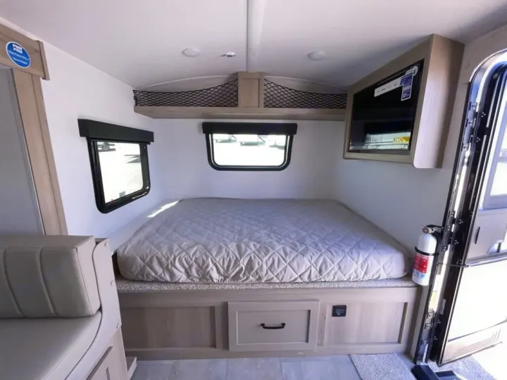 A compact RV rental interior featuring a bed, side windows, overhead storage, and a wall-mounted TV. Ready for your next trip.. Forest River RV Rockwood GEO Pro 2025