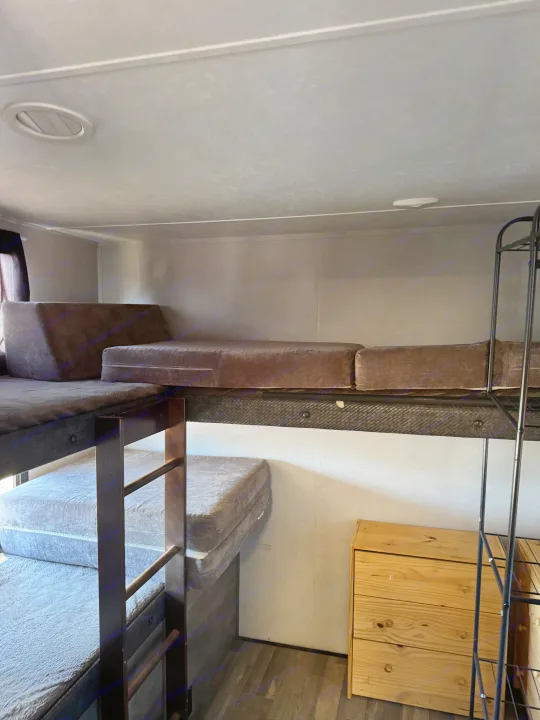 An RV rental interior featuring stacked bunk beds with cushions, a wood dresser, and metal shelving.. Forest River vibe 2020