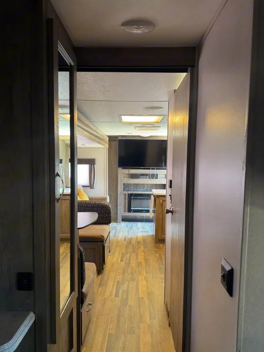 A spacious RV rental interior features a living area with wood-look flooring, a large TV, dinette, and cozy seating.. Forest River vibe 2020