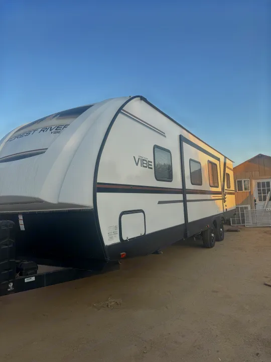 A white Forest River Vibe travel trailer, ready for RV rental adventures, parked on a dirt lot.. Forest River vibe 2020