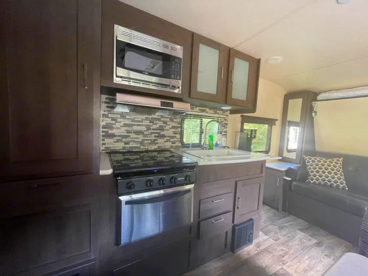 Stylish RV rental interior showing a full kitchen with stainless steel microwave, stove, sink, and a comfortable living space.. Forest River Wildwood X-Lite 2018