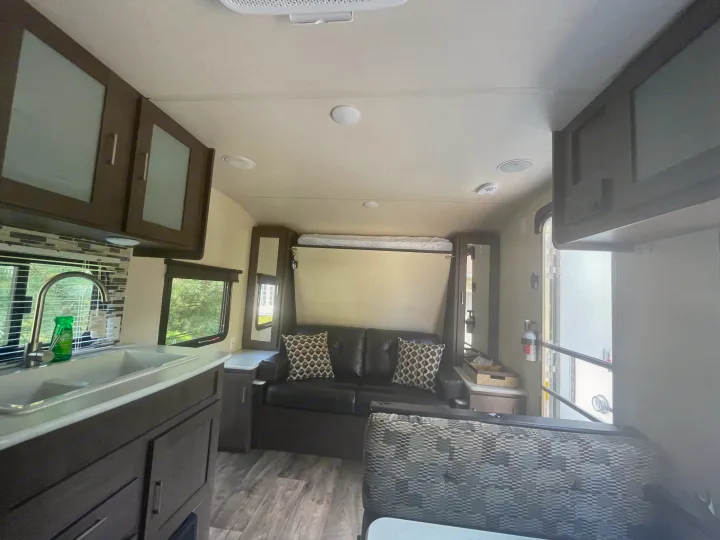 Modern RV rental interior with kitchen, black sofa, and fold-down bed. Features wood-look flooring and ample storage.. Forest River Wildwood X-Lite 2018