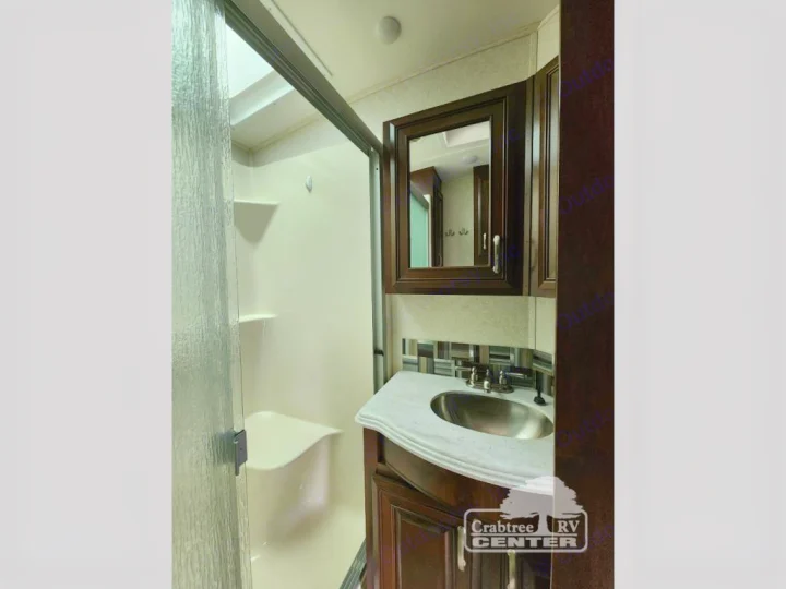 RV rental bathroom featuring a glass-enclosed shower with seat & shelves, plus a vanity with sink and mirrored cabinet.. Jayco Designer 39RE 2017