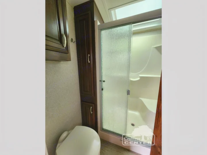 RV rental bathroom: Compact design featuring a toilet, dark wood cabinets, and a modern shower with a sliding glass door.. Jayco Designer 39RE 2017