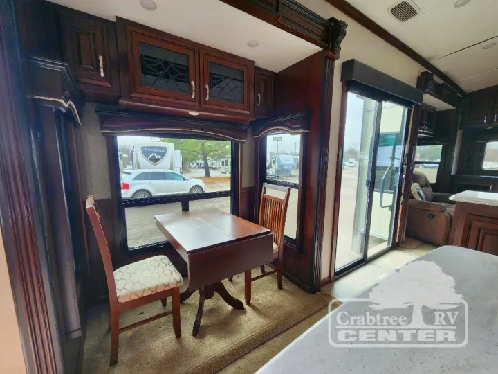 Warm-toned RV rental interior: dining area, wood cabinets, & large windows revealing outdoor views. Ideal for travel.. Jayco Designer 39RE 2017