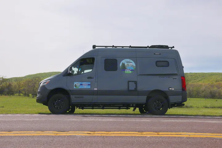 Gray Winnebago Revel 4x4 RV rental van on a road. Ready for smart adventures amidst green hills.. Mercedes Winnebago Revel 2023