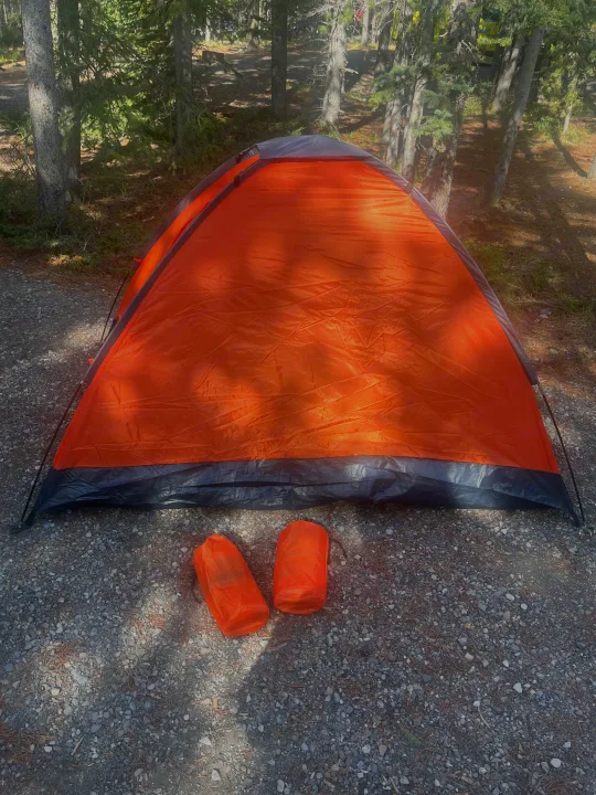 Bright orange tent and camping gear on a gravel campsite, ready for your RV rental adventure.. Sunset Park RV SunRay 2025