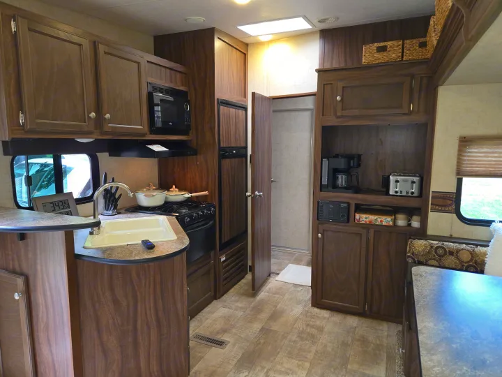 Inside an RV rental: a compact kitchen with wood cabinets, sink, stove, microwave, and fridge, plus a cozy living area.. KZ Sportmen Sportster Toyhauler 2015