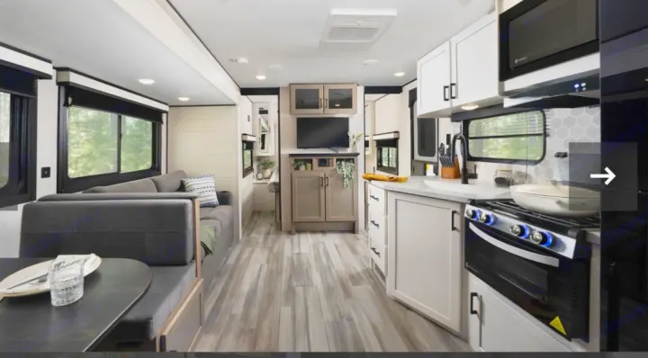 Modern RV rental interior with bright kitchen (stove, microwave, sink), dining area, cozy sofa, and TV, offering ample living space.. Jayco 267BHS 2025