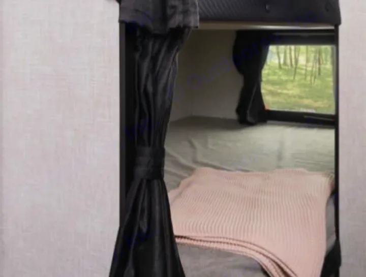 A comfortable bunk bed inside an RV rental, featuring a grey mattress, pink blanket, and a window to nature.. Jayco 267BHS 2025