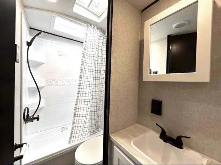 This RV rental offers a compact bathroom with a shower/tub combo, toilet, and a vanity sink with mirror.. Jayco 267BHS 2025