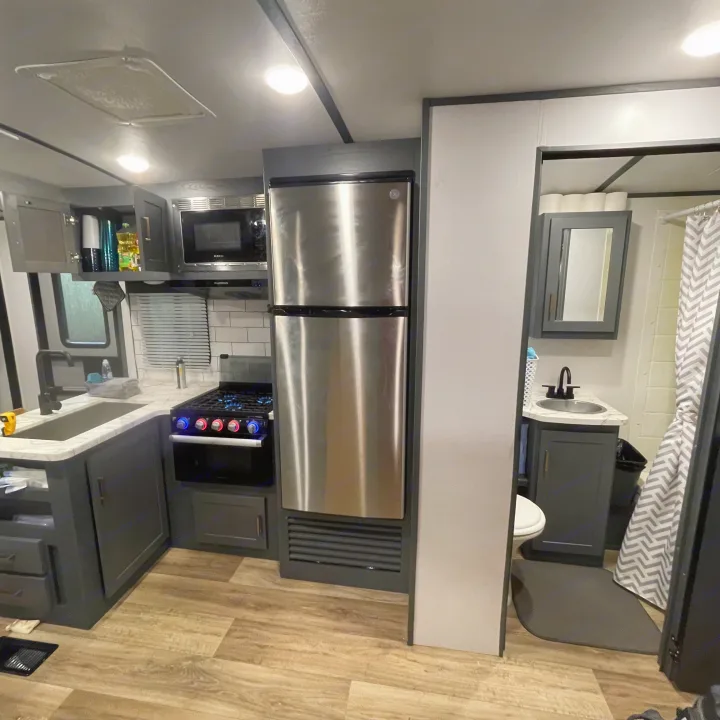 Inside an RV rental: A modern kitchen with stainless steel appliances, dark cabinetry, and a clean bathroom visible through the doorway.. Keystone RV Bullet Ultra Lite 2022