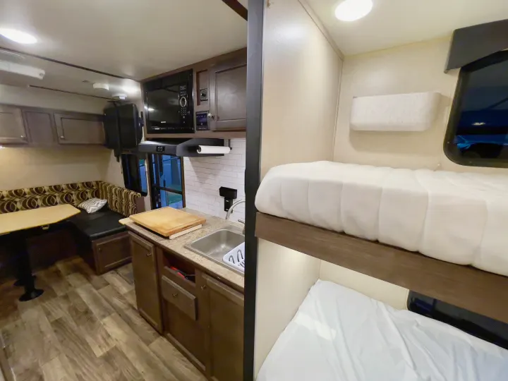 Spacious RV rental interior featuring a kitchen with a sink, microwave, a dinette, and cozy bunk beds.. Sunset Park RV Sun Lite 2019