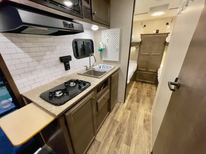 Inside this RV rental, discover a functional kitchen with a stove and sink, plus a hallway leading to cozy bunk beds and storage.. Sunset Park RV Sun Lite 2019