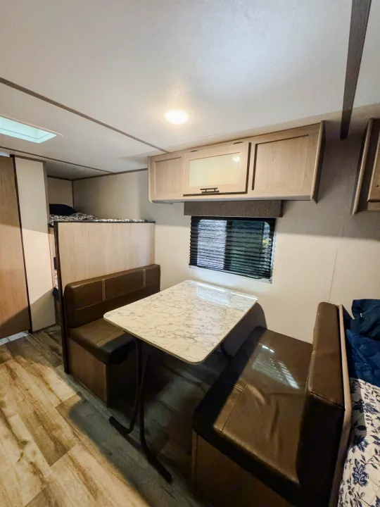 Inside this RV rental: a bright interior featuring a marble-look dining table, brown booth seats, overhead cabinets, and bunk beds.. Dutchmen Coleman Lantern LT 2023