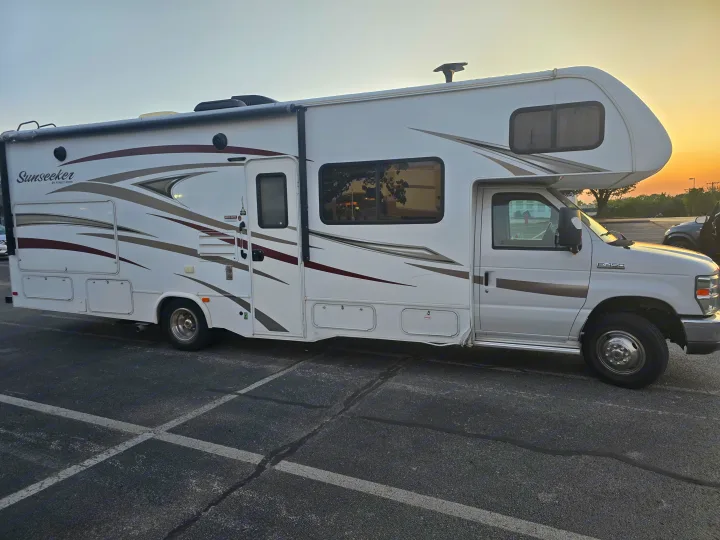 White and brown Sunseeker Class C rv rental, a Ford E-450 model, parked at dusk.. Forest River Sunseeker 2016
